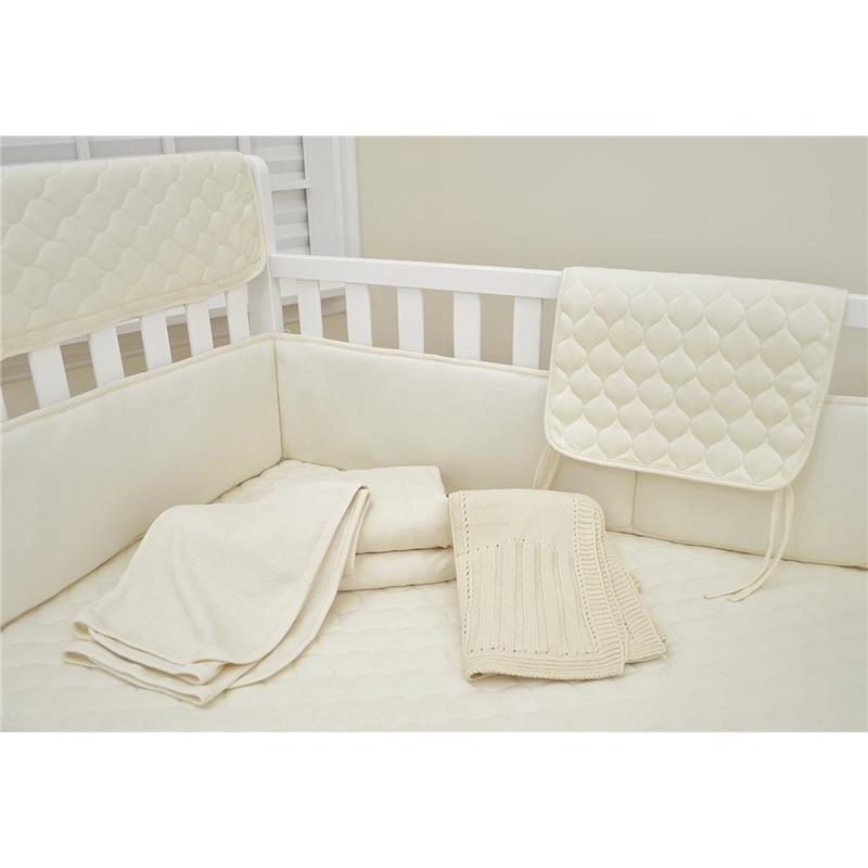 Thermal/waffle swaddle blanket made with organic cotton in natural color laid in a crib, alongside other soft, cream-colored bedding.