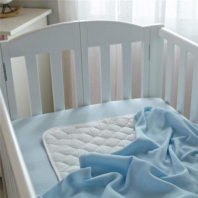 100% cotton thermal waffle swaddle blanket in blue, neatly draped over a crib mattress with a quilted mattress pad.
