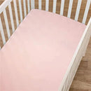 Fitted mini crib sheet in blush color, made of 100% cotton jersey, placed in a white wooden crib.
