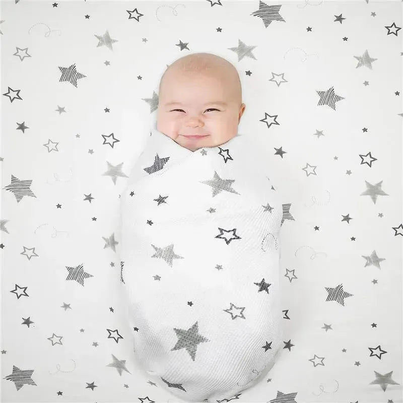 Smiling baby swaddled in a white knit blanket with a star pattern, resting on a matching crib sheet.