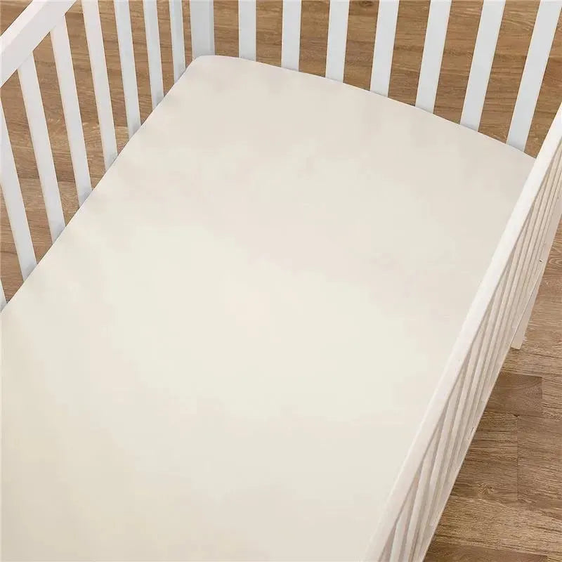 Ecru fitted crib sheet made of 100% natural cotton jersey knit, placed inside a white wooden crib.