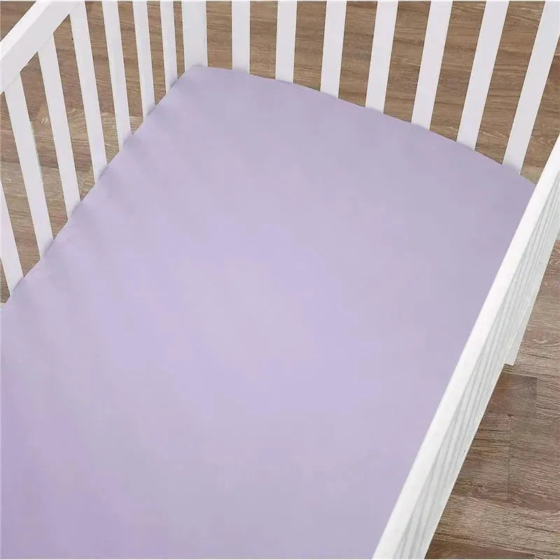 Fitted crib sheet in lavender color placed in a white crib, set on a wooden floor.