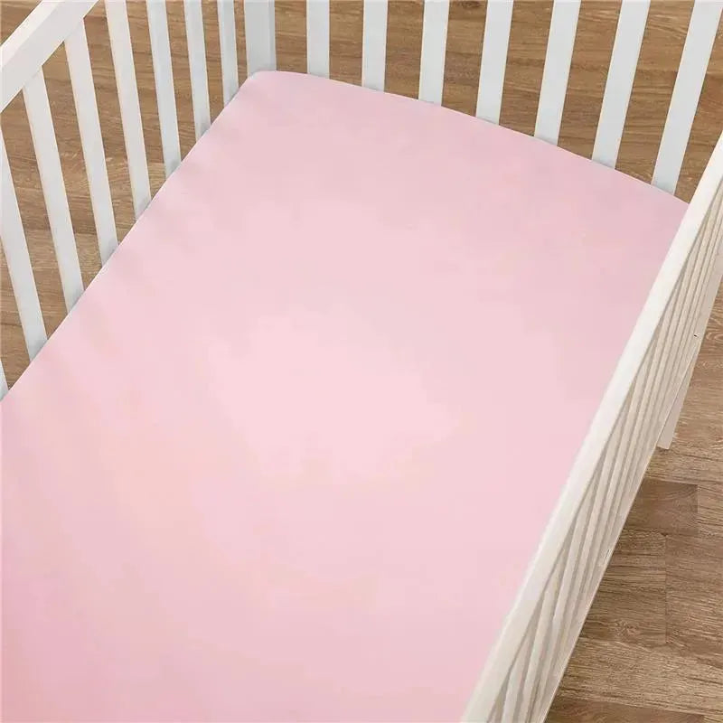 100% natural cotton jersey knit fitted crib sheet in pink, laid in a wooden crib on a wooden floor.