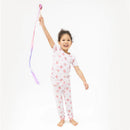 Smiling girl wearing a pink floral short sleeve loungewear set, playing with a colorful ribbon in a bright setting.