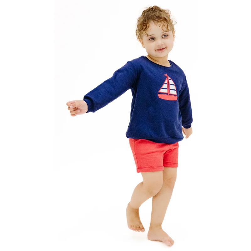 Baby wearing a navy sweatshirt with a sailboat applique and red paperbag shorts, smiling and posing.