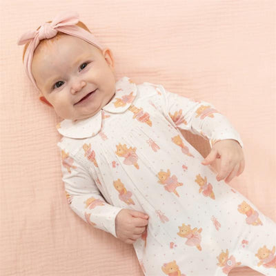 Baby wearing a white footie with teddy bear ballerina print, smiling on a pink background.
