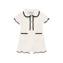 White collared romper for baby girls featuring black trim, button closure, and two front pockets.