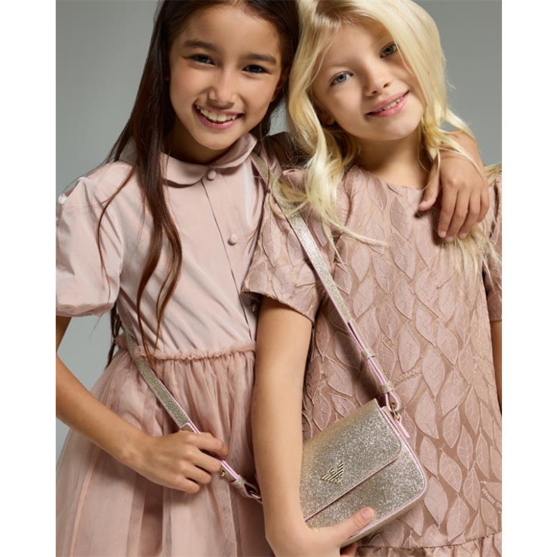 Two girls smile while wearing stylish pink dresses, with one girl holding a shiny, glittery handbag.