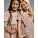 Two girls smile while wearing stylish pink dresses, with one girl holding a shiny, glittery handbag.