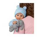 Baby boy doll wearing a light blue bear-hat, holding a grey stuffed dog, with a background person in a pink shirt.