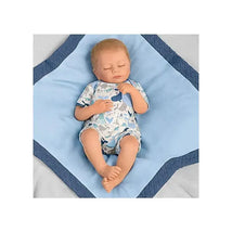 Breathing baby boy doll dressed in a playful onesie, resting on a blue quilted blanket.