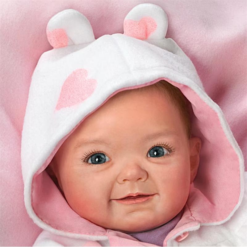 Ashton Drake Cutest Baby Portrait Savana Baby Doll wearing a white hood with pink hearts, smiling with blue eyes.