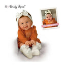 Lilah Baby Girl doll by Ashton Drake dressed in an orange outfit with ruffle sleeves and a white headband, smiling.