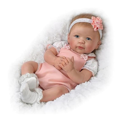 Lifelike silicone baby doll in a pink outfit with a floral headband, resting on a fluffy white surface.