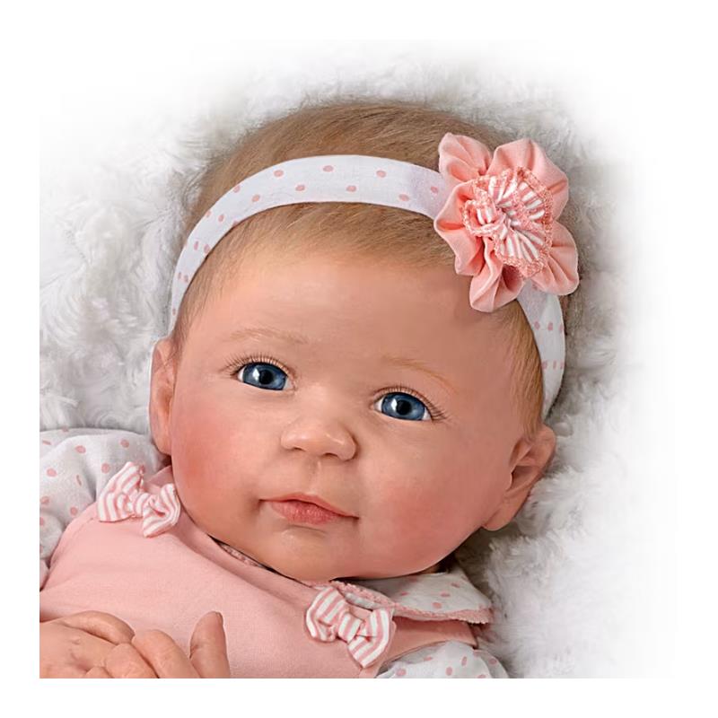 Lifelike silicone baby doll by Ashton Drake, featuring blue eyes, a pink outfit, and a floral headband.