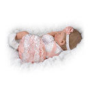 Lifelike silicone baby doll by Ashton Drake, featuring a polka dot dress, pink accents, and a floral headband, resting on fluffy white fabric.