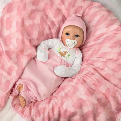 Lifelike baby girl doll dressed in a pink deer-themed outfit, lying on a pink camouflage blanket with a pacifier.