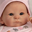 Realistic baby doll with brown eyes, wearing a pink outfit with elephant designs, and a matching pink hat.