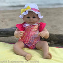 Ashton Drake Little Peanut Baby Doll Girl wearing a colorful swimsuit with a hat, sitting on a sandy surface.