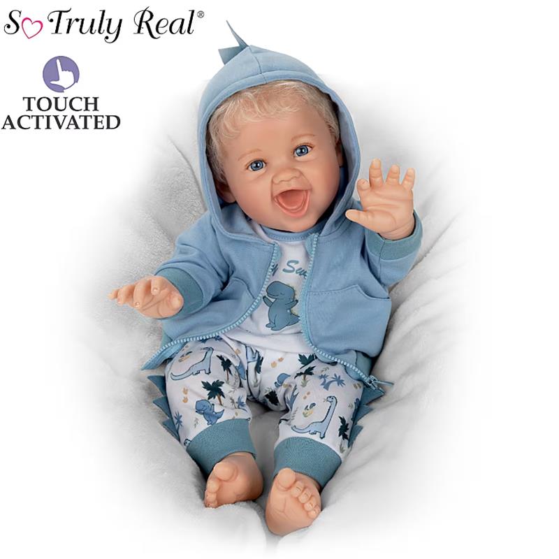 Touch-activated Ashton Drake dinosaur baby boy doll wearing a blue hoodie and playful dinosaur-themed pajamas, smiling and waving.