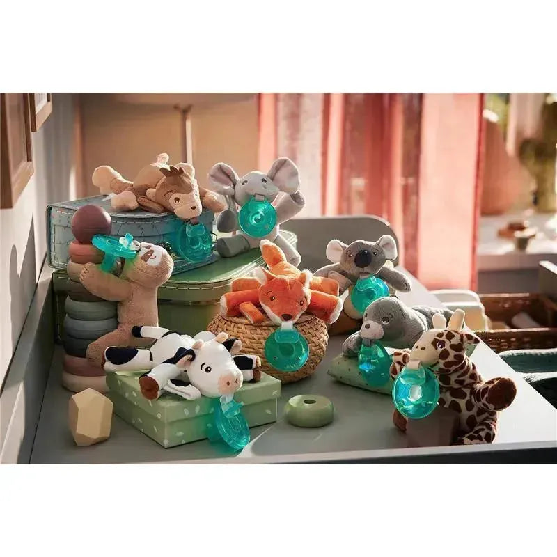 A collection of plush animal toys, including a fox and elephant, each holding a teal pacifier, arranged on colorful storage boxes.