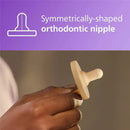 Light yellow Avent Soothie pacifier with symmetrical orthodontic nipple, held in a hand, on a gradient background.