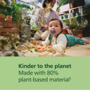 Baby playing on a mat with a blue pacifier, surrounded by toys and plants, highlighting eco-friendly packaging.