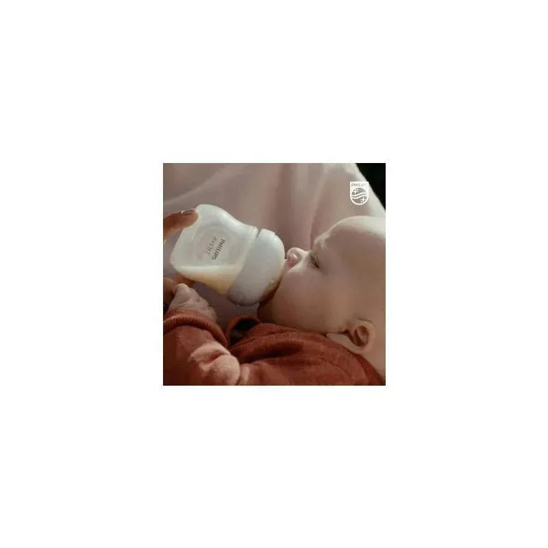 A baby in a red outfit is feeding from an Avent 4oz baby bottle with a natural response nipple.