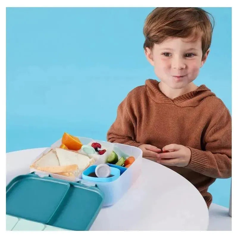 Child sitting at a table with a B.box lunchbox in Ocean Breeze color, filled with fruits, vegetables, and sandwiches.