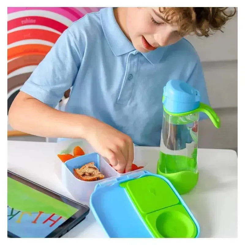 A child in a blue shirt uses a B.box Mini Lunchbox in Ocean Breeze colors, filled with healthy snacks, next to a water bottle.
