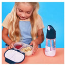 A young girl examines a B.box Snackbox in blue slate, filled with snacks, alongside a matching water bottle on a table.