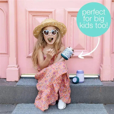 Girl in sunglasses and a straw hat holds a B.box So Bunny insulated food jar while eating, with pink doors in the background.