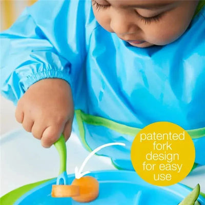 Toddler using the B.box Banana Split Cutlery Set to cut a slice of fruit, highlighting the patented fork design for easy use.