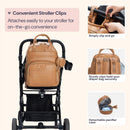 Light brown vegan leather diaper bag attached to a stroller, featuring clips for easy attachment and a detachable pacifier case.
