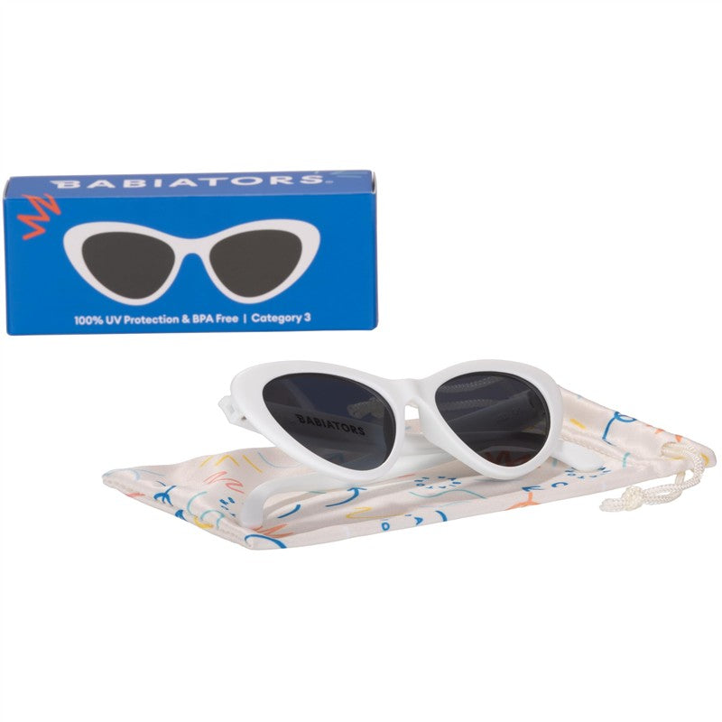Children’s cat-eye shaped white UV sunglasses by Babiators, displayed on a colorful protective pouch and box.