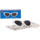 Children’s cat-eye shaped white UV sunglasses by Babiators, displayed on a colorful protective pouch and box.