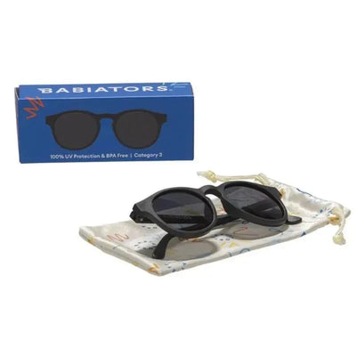 Jet black Babiators sunglasses for kids aged 3-5, displayed on a protective pouch with a blue box featuring UV protection details.