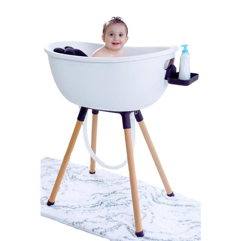 Luxury white baby bathtub on a wooden stand, with a smiling baby inside and a bottle of soap on the side.