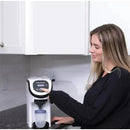 Woman using the Baby Brezza Formula Pro Mini on a kitchen counter to prepare formula in a clear container.