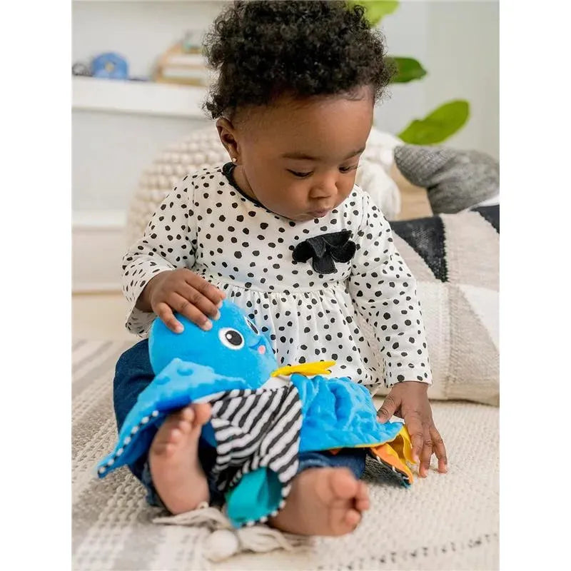 A baby in a polka dot shirt plays with a colorful Baby Einstein Sensory Plush Octopus, engaging with its textures.