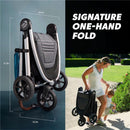 Baby Jogger City Mini GT3 stroller in Sierra Sand, folded for easy transport, with a woman carrying it and holding a child.