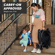 Compact Baby Jogger City Tour 2 stroller in eco black held by a woman with a child on stairs, showcasing its portability.