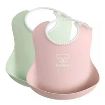 Two Babybjorn baby bibs in powder green and powder pink, featuring a catch pocket and soft, flexible design.