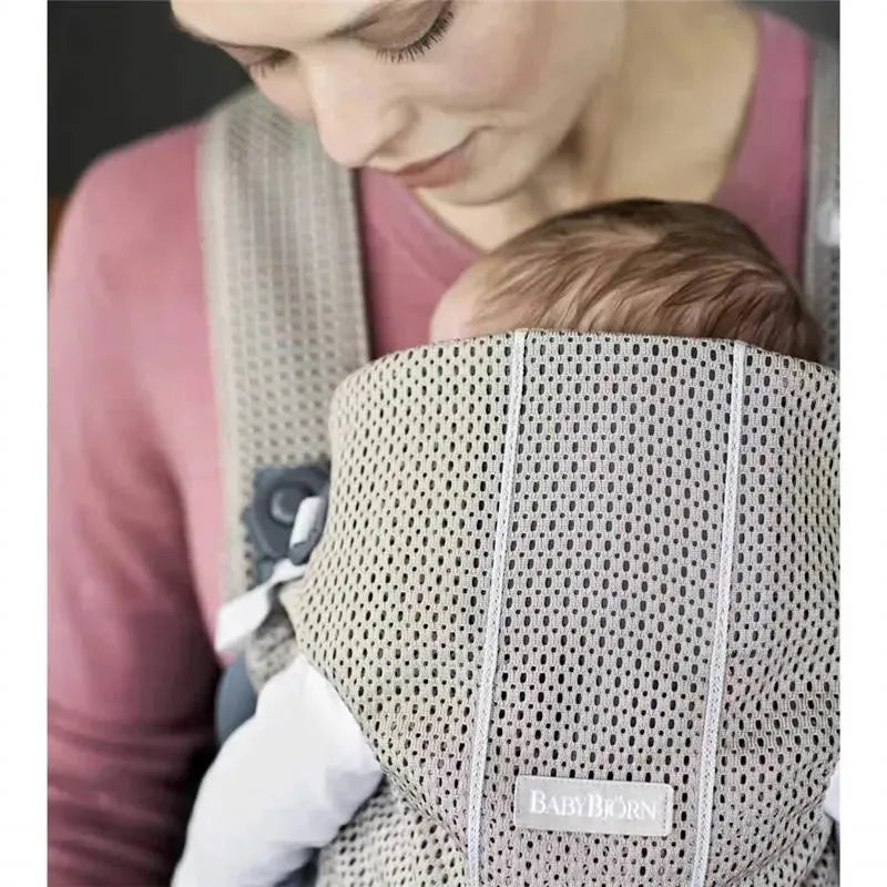 Babybjorn Baby Carrier Mini in gray beige, featuring a parent holding a baby snugly against their chest.