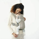 Babybjorn Baby Carrier Mini in gray beige, worn by a smiling woman holding a baby securely against her chest.