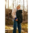Mother holding a baby in a black Babybjorn carrier cover while standing in a forest setting.