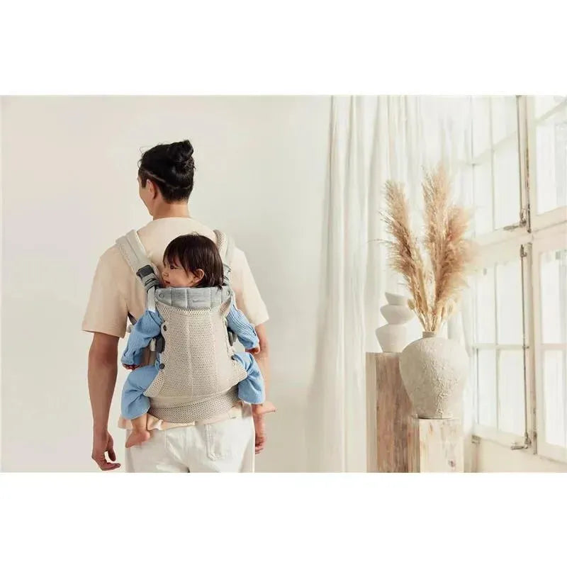 BabyBjorn Baby Carrier Harmony in cream color, worn by a person carrying a smiling child on their back.