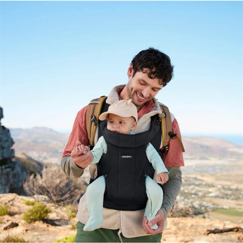Father carrying a baby in a Babybjorn Baby Carrier Hold Mesh, dressed in a scenic outdoor location.