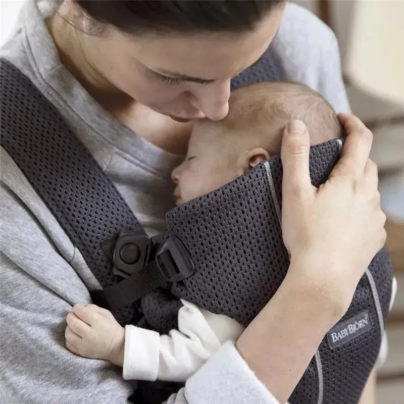 Babybjorn Baby Carrier Mini in anthracite, worn by a mother holding her sleeping baby, showcasing a soft, breathable mesh design.