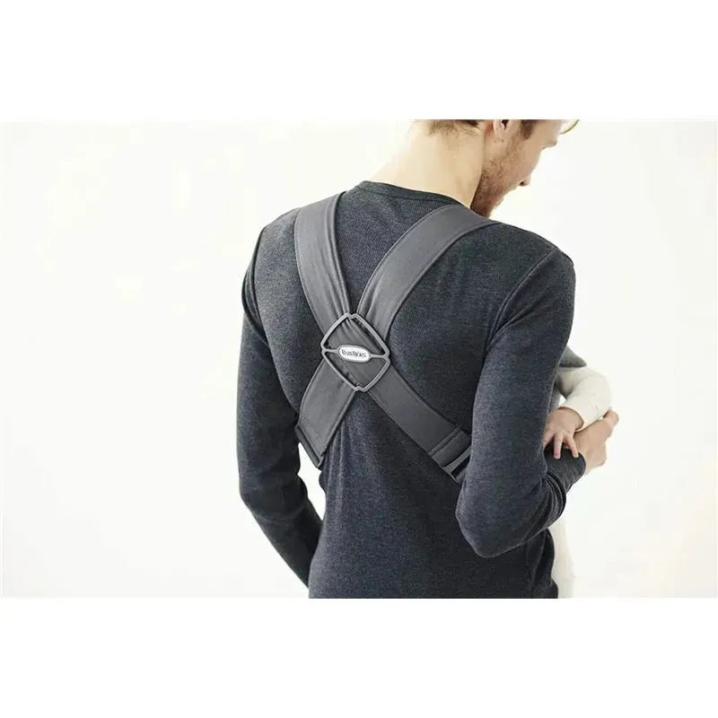 BabyBjorn Baby Carrier Mini in Dark Gray is worn by a person holding a baby; features adjustable straps and a secure design.